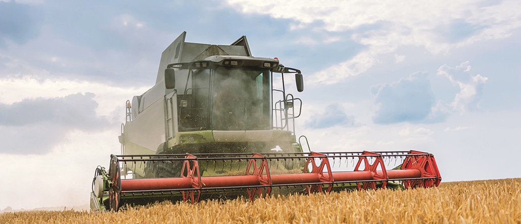 Modern agricultural field equipment, a combine harvester, working in a wheat field, representing a major capital investment for a farming operation.